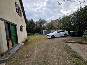 Guests can park their vehicle in the driveway, with a small shed and green door nearby.