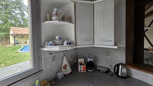 Een keuken met witte kasten, een inbouwplank met wit en blauw bloemendecor servies, een koffiezetapparaat, een waterkoker en een klein raam met uitzicht op een achtertuin.