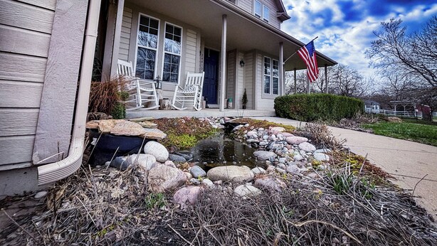A two-story house with a porch, a small pond, and an American flag.