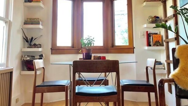 A room with a wooden ceiling, a large window, a dining table with chairs, and a wall-mounted shelf with books and decorative items. - Close-in Private Getaway in the trees of Portland (Portland)
