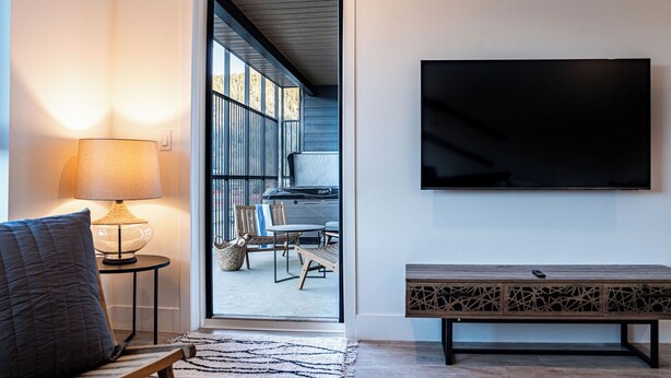 A modern living room with a sofa, a lamp, a TV, and a bench. - Drop In Condo by Revelstoke Vacations (Revelstoke)