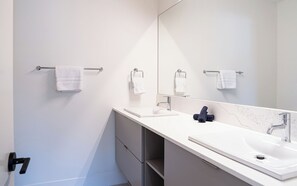 A modern bathroom with a white sink, a large mirror, and two towel racks. - Drop In Condo by Revelstoke Vacations (Revelstoke)