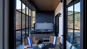 A balcony with a hot tub, wooden chairs, and a table with cups. - Drop In Condo by Revelstoke Vacations (Revelstoke)