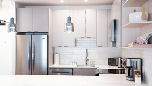 A modern kitchen with stainless steel appliances, white cabinetry, and pendant lighting. - Drop In Condo by Revelstoke Vacations (Revelstoke)