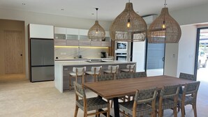Una cocina moderna con una isla central, luces colgantes y un comedor con una mesa de madera y sillas estampadas.
