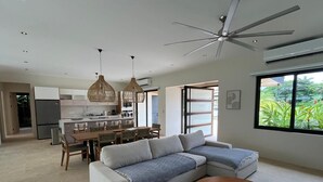 Una sala moderna con un sofá modular, una mesa de comedor y sillas, una mesa de centro redonda y un ventanal con vistas a zonas verdes.