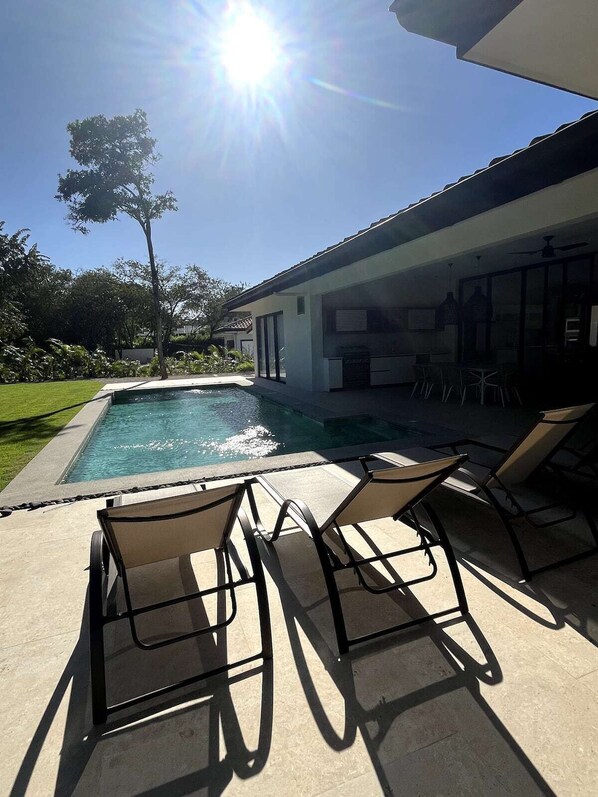 Ein Swimmingpool mit Liegestühlen, eine Terrassenfläche und ein Gebäude mit großen Fenstern.