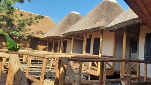A rustic accommodation with thatched-roof huts, wooden beams, and a wooden deck. - Sunscape lodge  (Fort Portal)