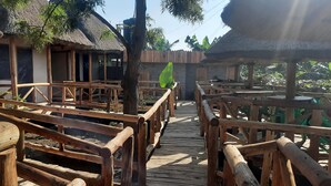 A wooden deck leading to a thatched-roof building with multiple windows and doors. - Sunscape lodge  (Fort Portal)