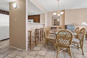 A dining area with wicker chairs and a glass table, a kitchen with wooden cabinets, and a white refrigerator.