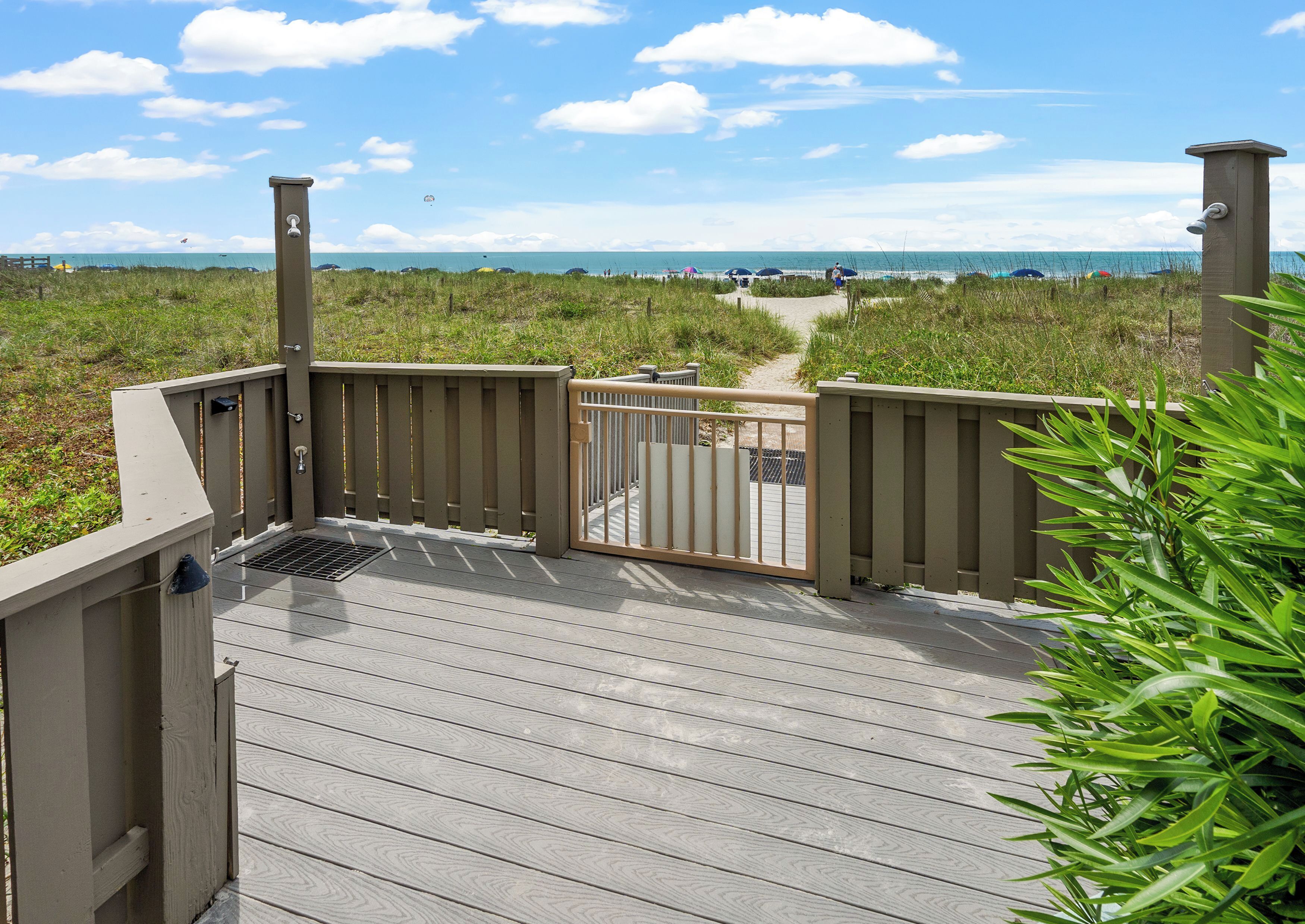 A wooden deck with a metal gate leading to a beach path.