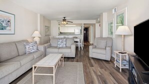 A living room with a sofa, armchairs, a coffee table, a TV, and a ceiling fan. - Shoreham Towers 5C (North Myrtle Beach)