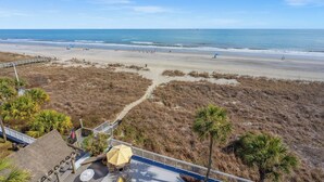 A beach view with a wooden deck, palm trees, and a boardwalk leading to the beach. - Shoreham Towers 5C (North Myrtle Beach)