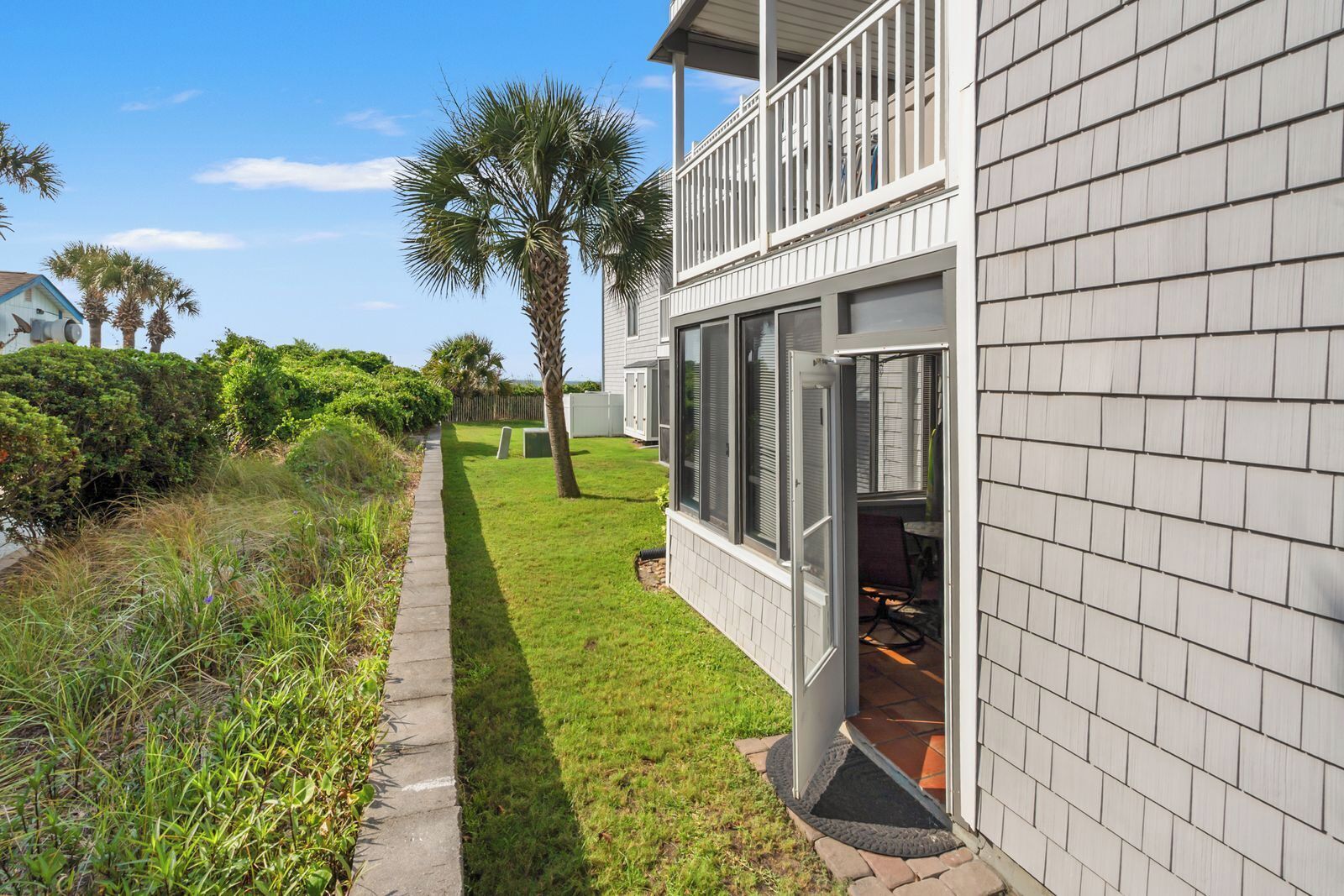 A two-story house with a balcony, a well-maintained lawn, and a palm tree.