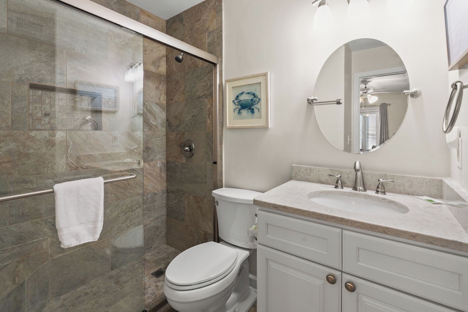 A modern bathroom with a glass-enclosed shower, a toilet, a sink with a vanity, and a mirror.