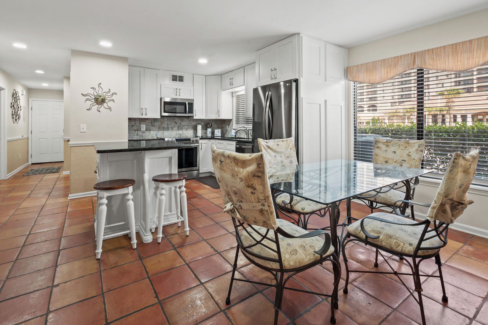 A modern kitchen with white cabinetry, stainless steel appliances, and a dining area with patterned chairs and a glass table.