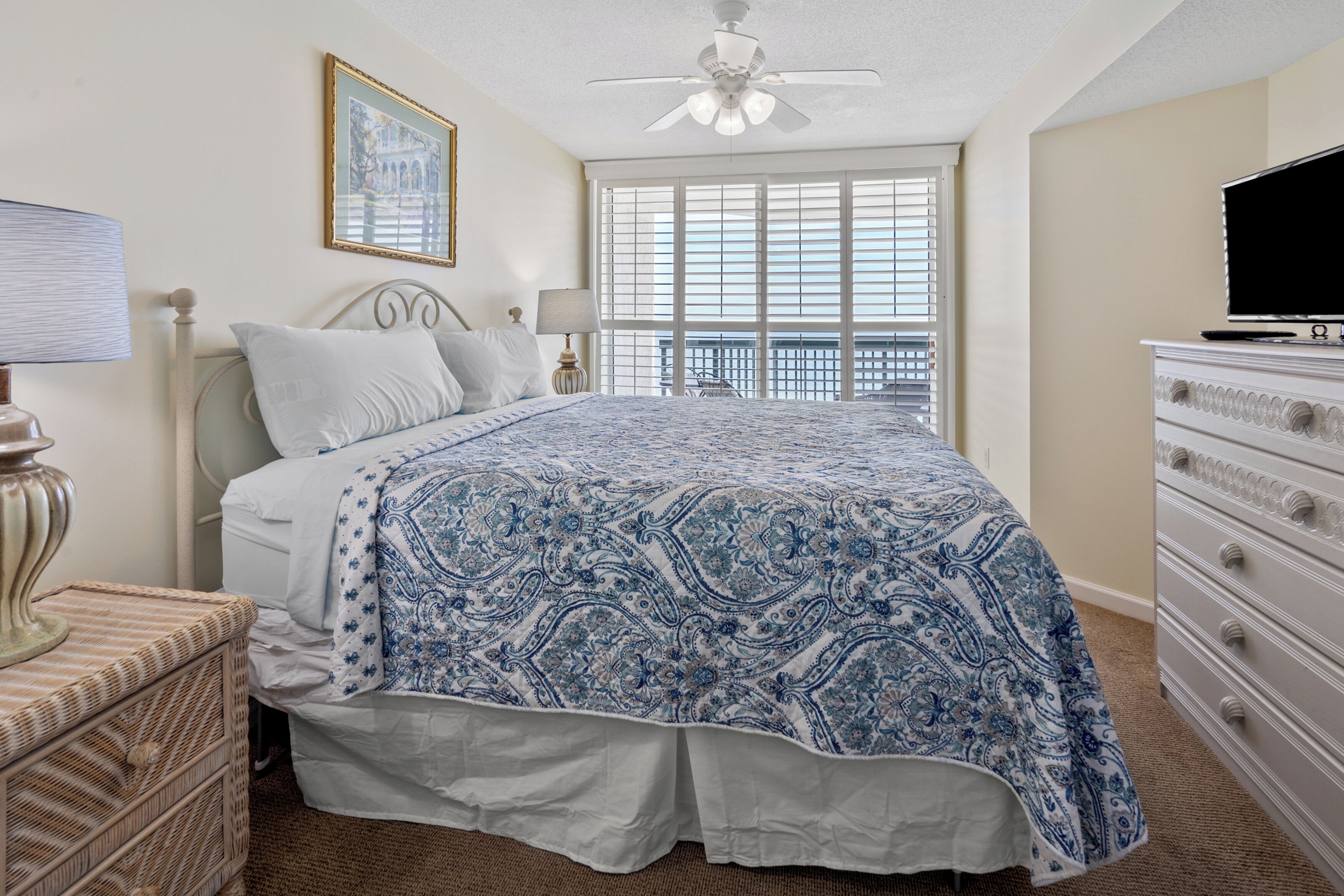 A bedroom with a bed, a dresser, a ceiling fan, a window with blinds, and a framed picture on the wall.