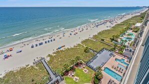 Un complejo turístico en la playa con piscina, sombrillas y un paseo marítimo.