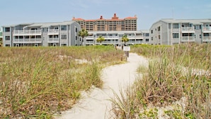 Un hotel affacciato sulla spiaggia, con edifici a più piani, un vialetto sabbioso e vegetazione costiera.