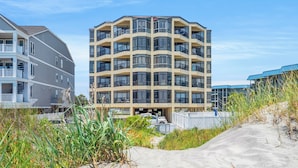 A multi-story building with balconies, a parking area, and a sandy foreground. - Sedgefield 102 (North Myrtle Beach)