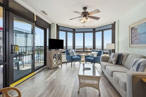 Un salón amplio con televisor grande, asientos cómodos, ventilador de techo y balcón con vistas.