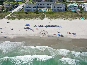 Una playa con sombrillas y gente, un edificio de varios pisos y vistas al océano.