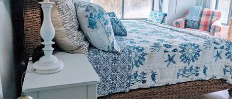 A bedroom with a large bed, a bedside table, a woven headboard, and a view of the outdoors through a window.