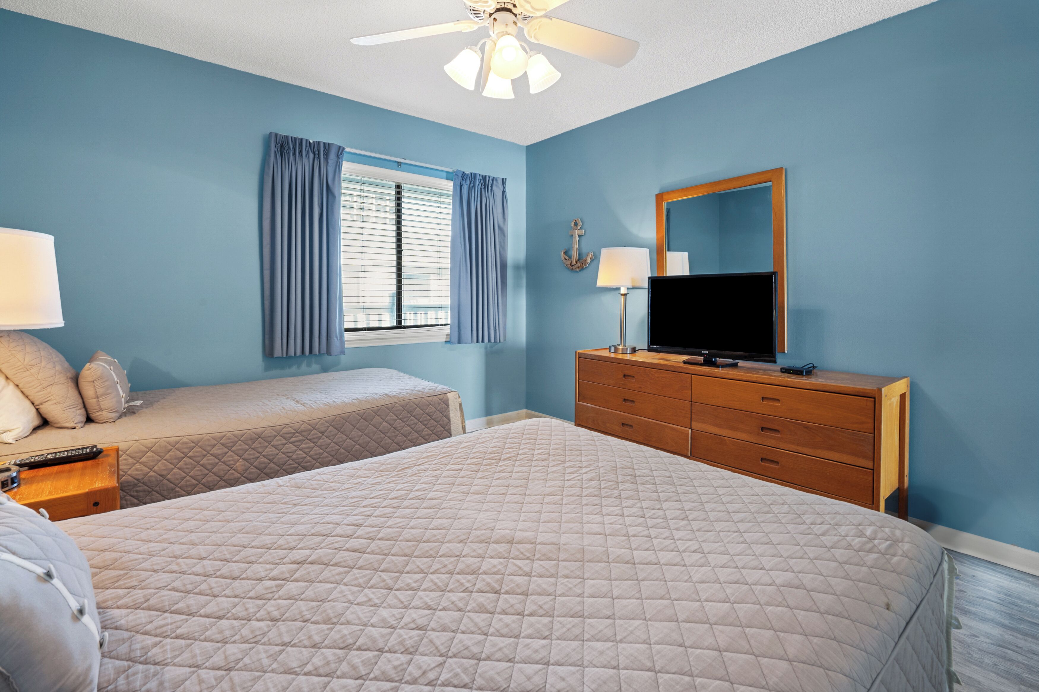 A bedroom with two beds, a dresser, a television, and a window with curtains.