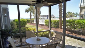 A covered patio with a table and chairs, overlooking a landscaped garden and a view of the ocean. - Sea Cloisters 101d (North Myrtle Beach)