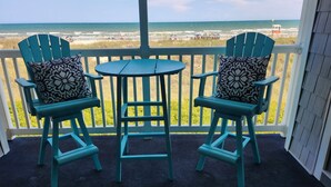 Un balcon avec deux chaises et une petite table, donnant sur une plage avec des vagues et des parasols.