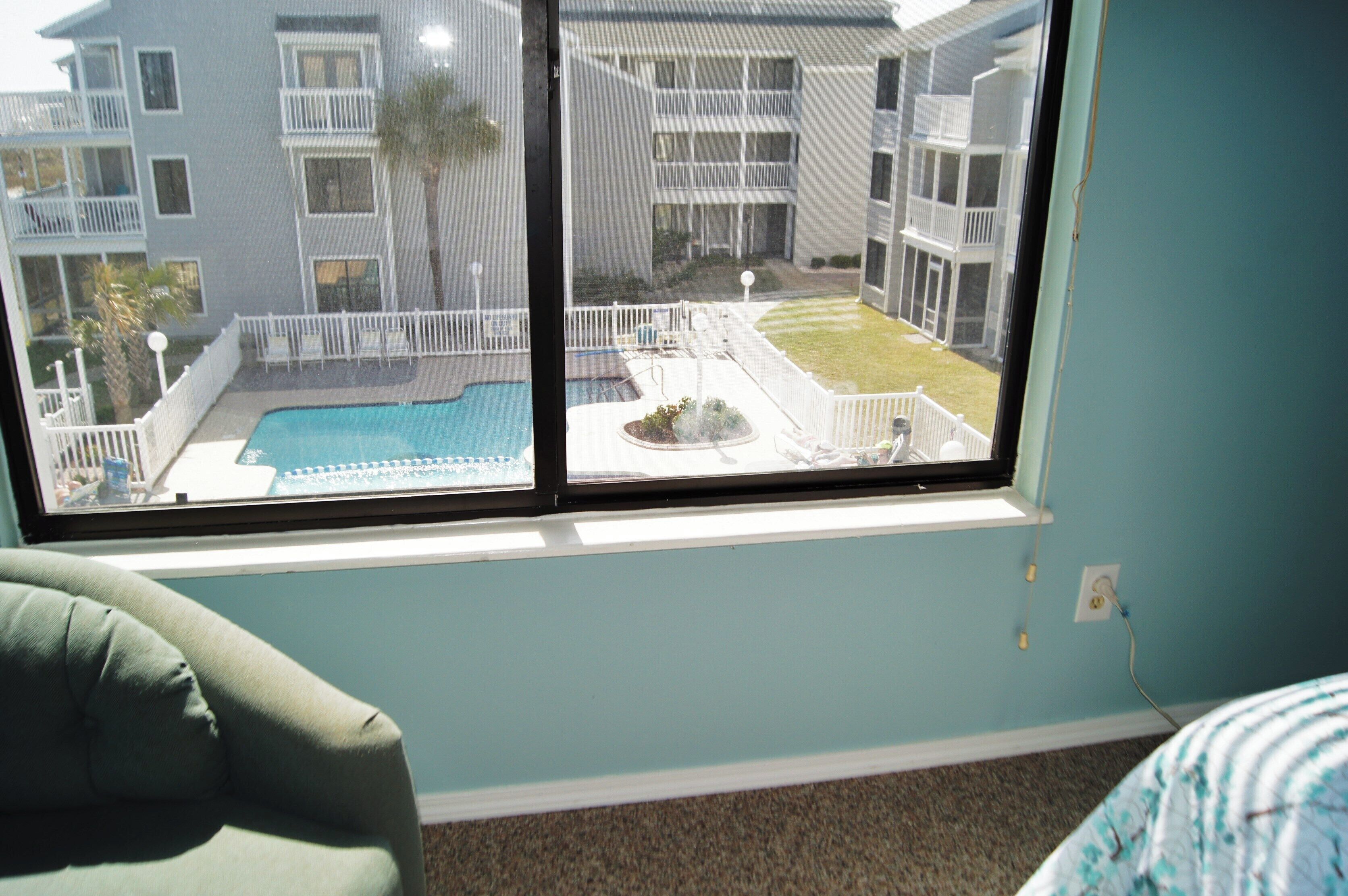 A room with a large window overlooking a swimming pool and a building with balconies.