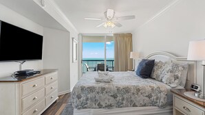 A hotel room with a bed, a television, a ceiling fan, a nightstand, and a view of the ocean. - Ashworth 1809 (North Myrtle Beach)