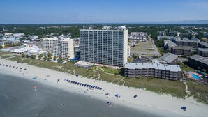 An aerial view of a coastal area with a large hotel complex, a beach with umbrellas, and a clear sky. - Ashworth 1809 (North Myrtle Beach)