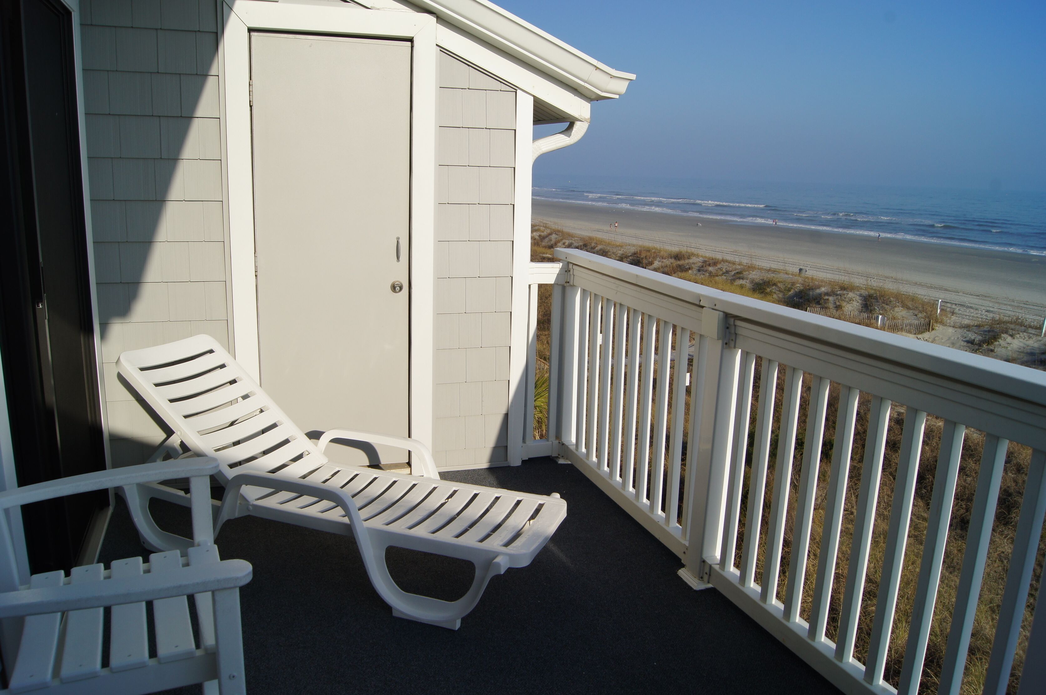 A balcony with white railings overlooking a beach.