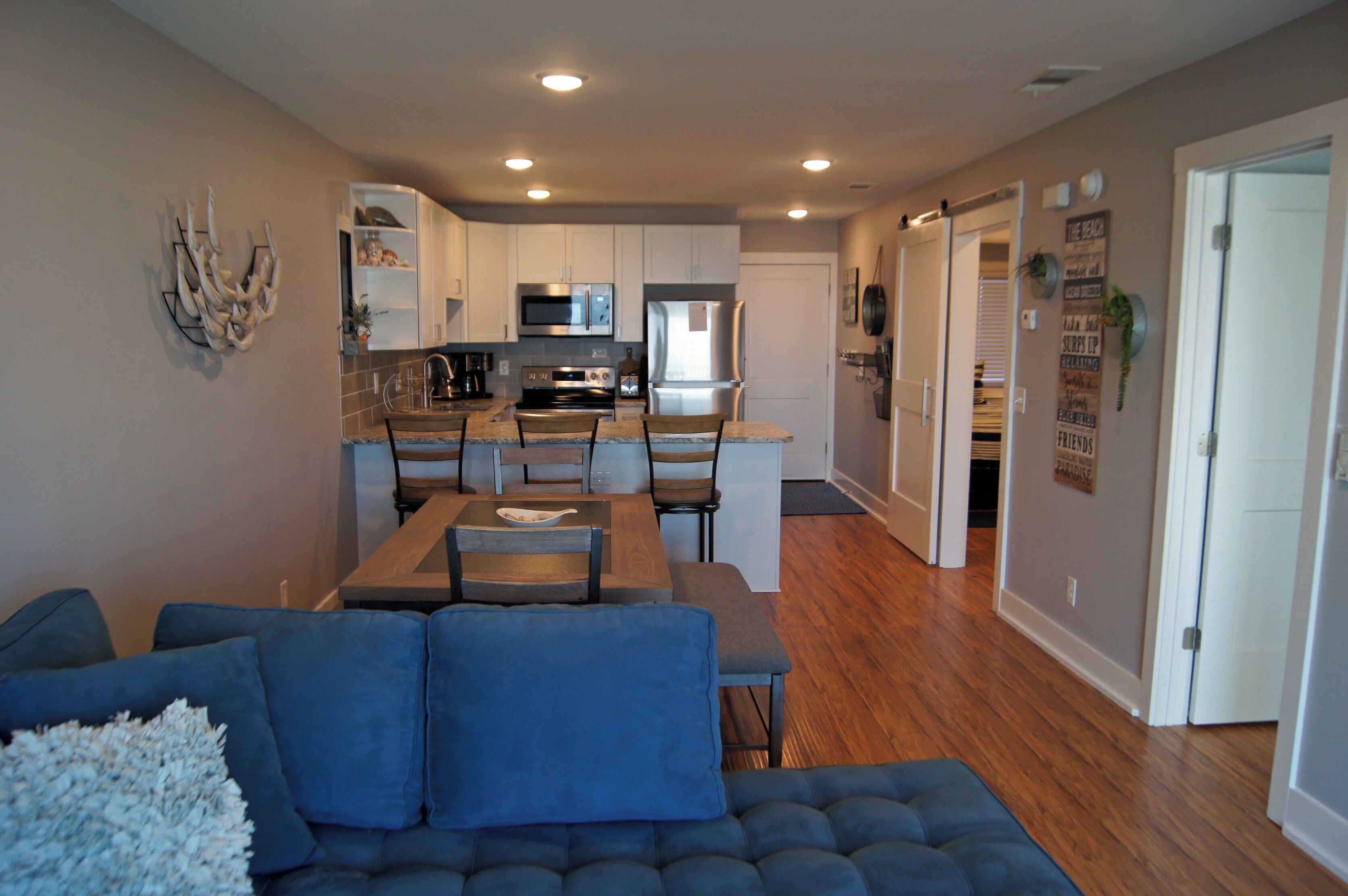 A modern kitchen with white cabinets, stainless steel appliances, and a dining area with a blue sofa and wooden table.