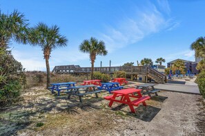 A beachside area with picnic tables, palm trees, and a wooden walkway leading to a building. - Avista Resort 1503 (North Myrtle Beach)