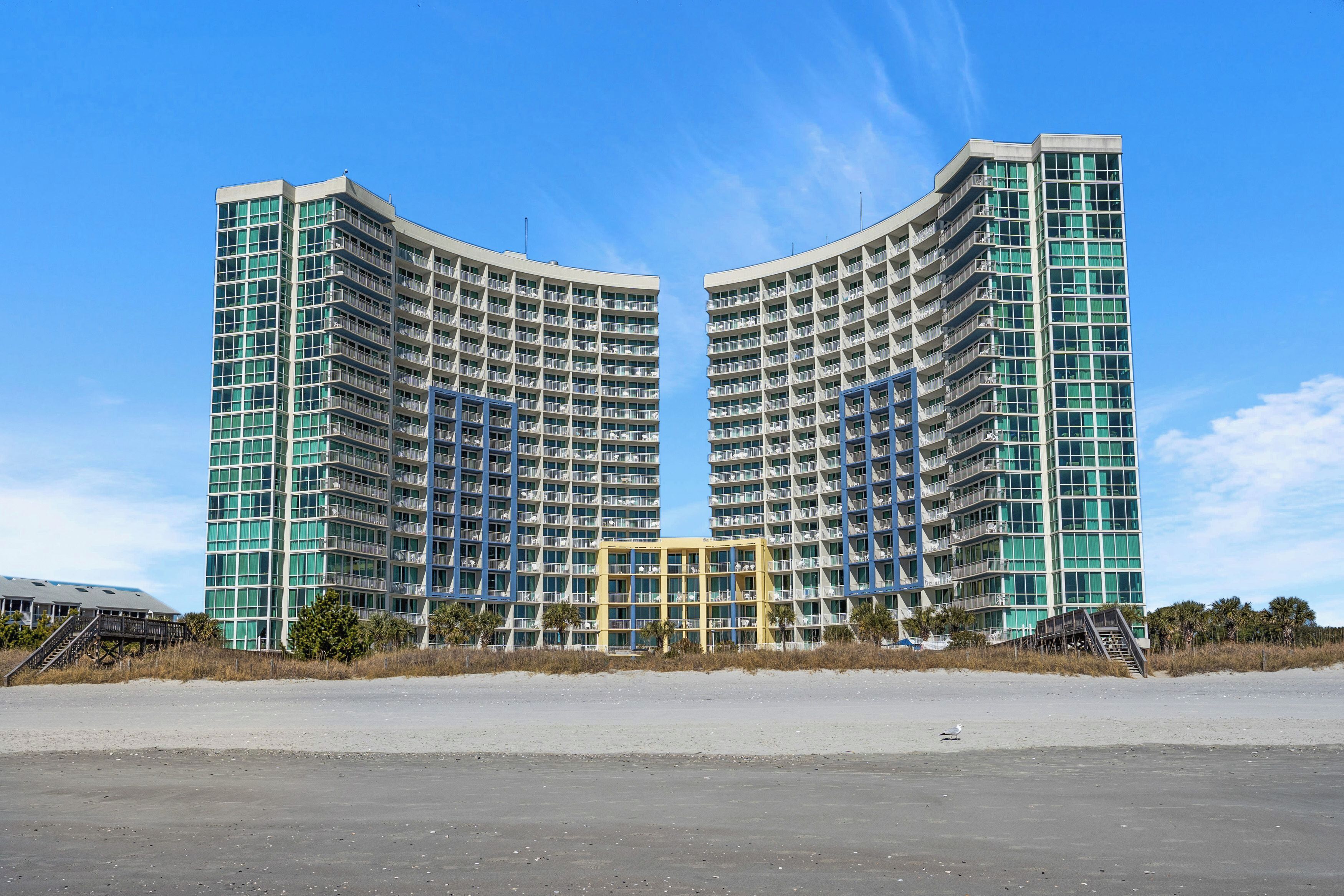 A large, modern hotel with a curved facade, multiple balconies, and a central entrance.
