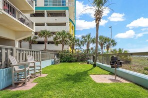 A hotel courtyard with a grassy lawn, outdoor seating, and a view of the ocean. - Shoreham Towers 2C (North Myrtle Beach)