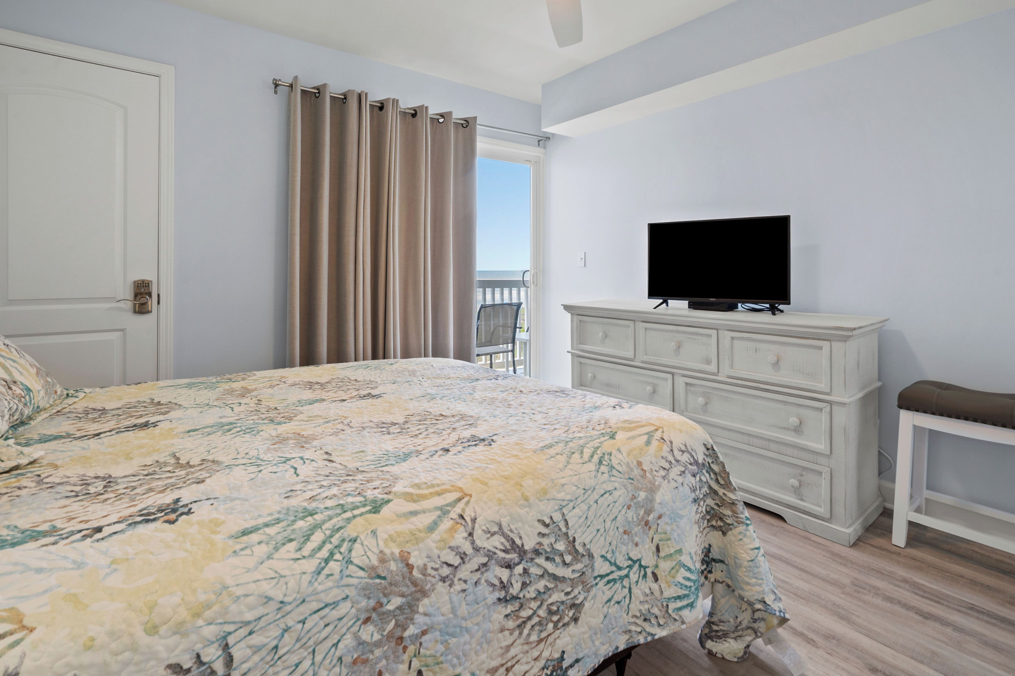 A bedroom with a bed, a television on a dresser, a chair, and a balcony door.