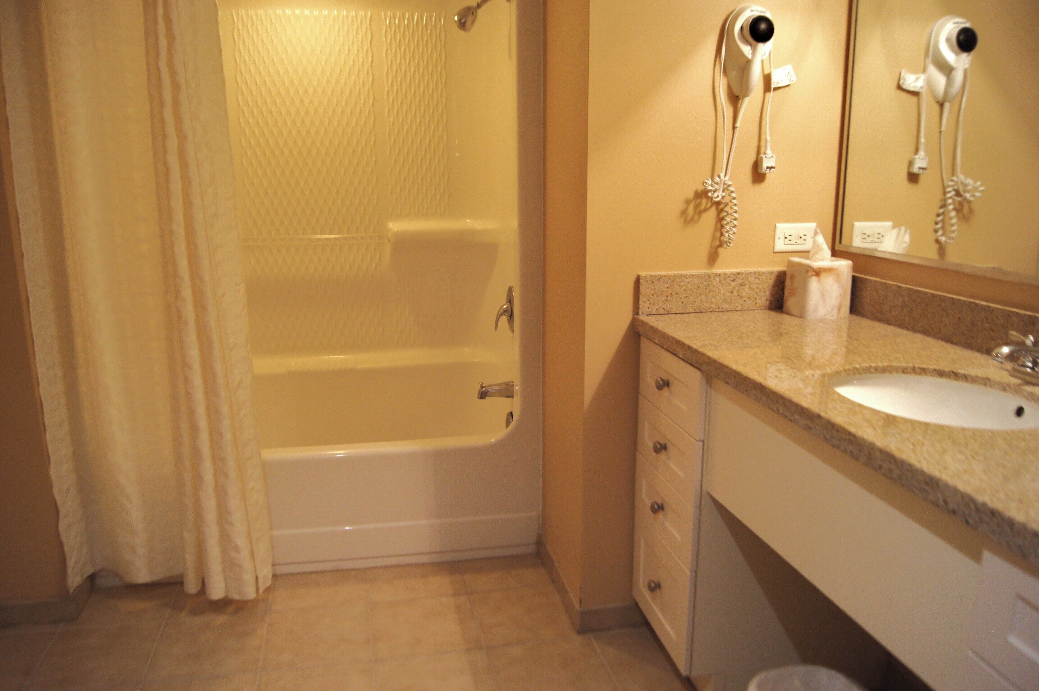 Une salle de bain équipée d’une baignoire, d’un lavabo, d’un miroir et d’un sèche-cheveux fixé au mur.
