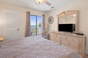 A bedroom with a large bed, a dresser, a television, and a view of the ocean through the window. - Sea Cloisters 303e (North Myrtle Beach)