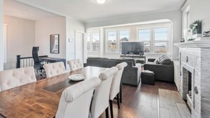 A spacious living room with a large wooden dining table, comfortable seating, a fireplace, and a television.