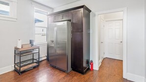 A kitchen with a stainless steel refrigerator, a wooden cart, and a red fire extinguisher.