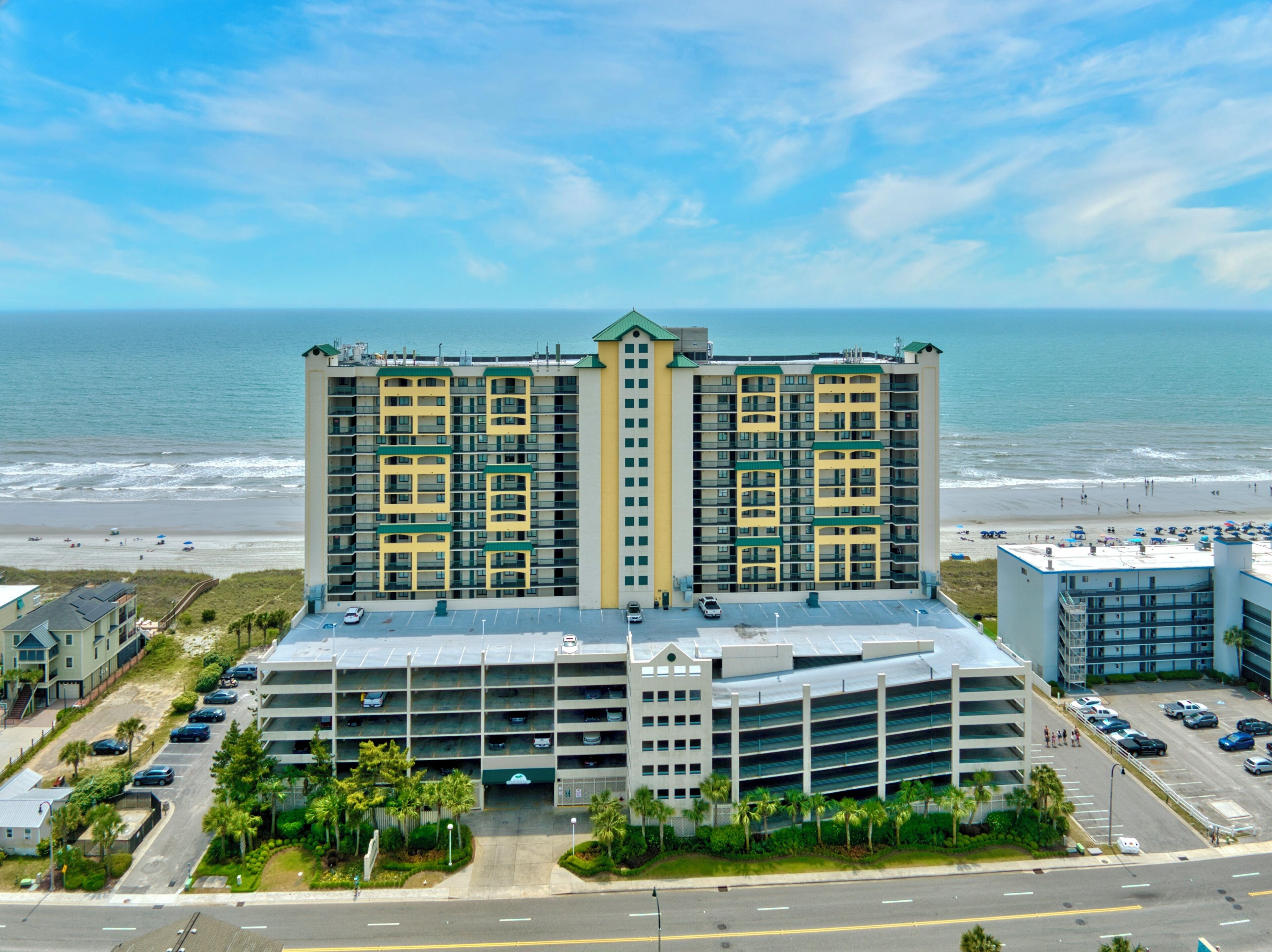 A multi-story hotel with a central courtyard, parking garage, and a beach view.