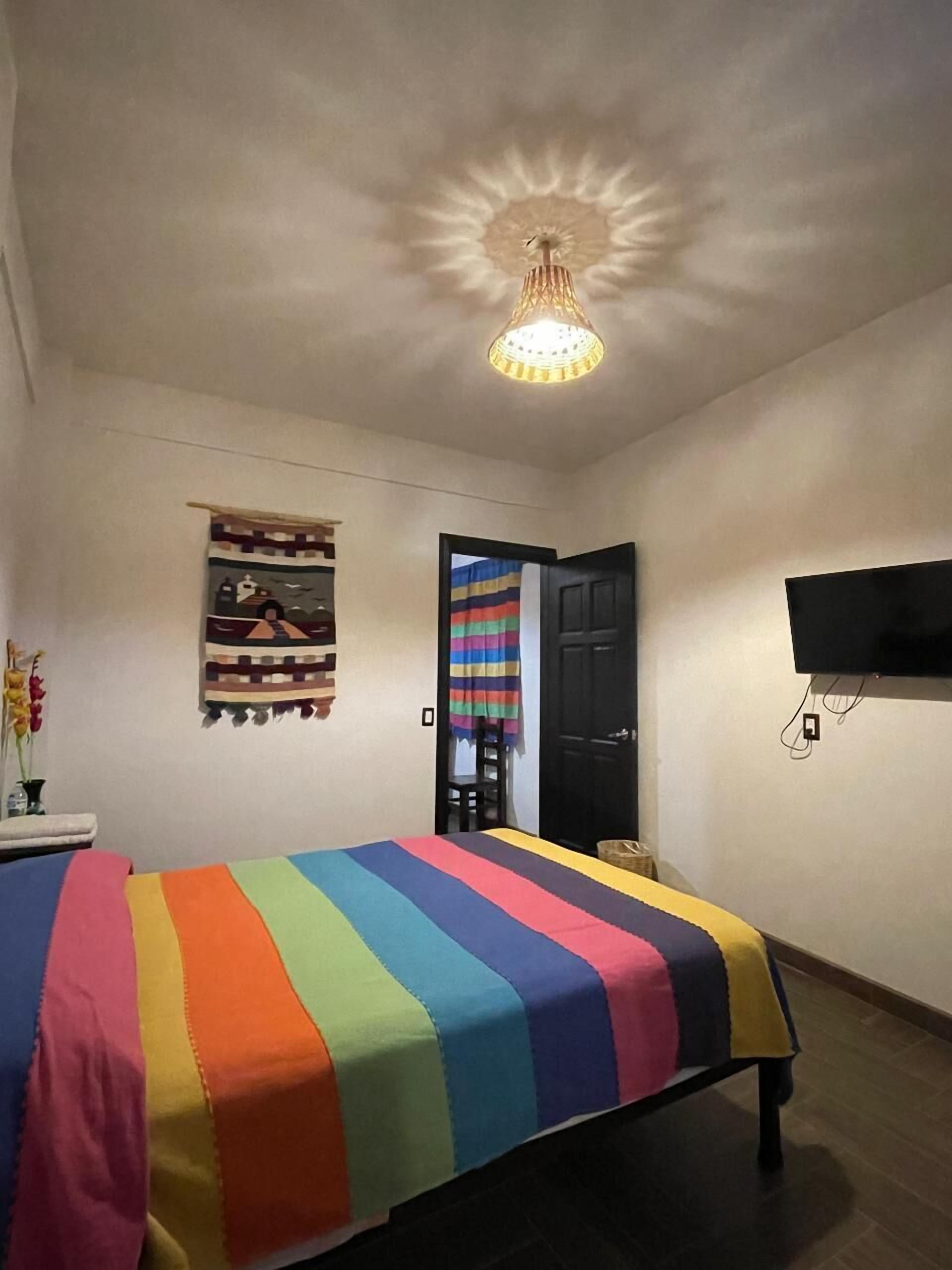 Ein Schlafzimmer mit einem Bett, einem an der Wand montierten Fernseher, einer Deckenleuchte und einer Tür.