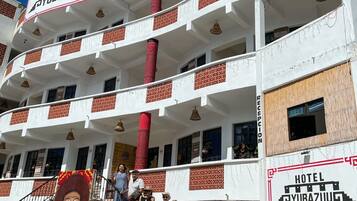 A multi-story hotel with balconies, a reception area, and a group of people gathered outside.