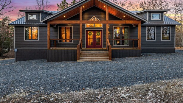 A two-story log cabin with a front porch, large windows, and a red door.