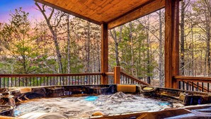 A hot tub with a wooden deck and railing, surrounded by trees.