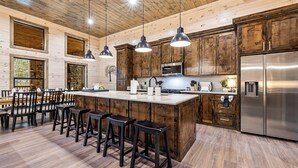 A spacious kitchen with wooden cabinets, a large island with stools, stainless steel appliances, and pendant lighting.