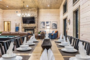 Enjoy meals in this cozy cabin-style dining area with a long table, comfortable seating, and a stone fireplace.